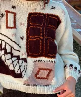 Sweater tejido en lana merino color crudo, con diseño artesanal en jacquard y bordados a mano de figuras geométricas en tonos marrón y terracota. Presenta cuello redondo, mangas largas y silueta relajada.