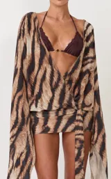 Vestido corto cruzado con estampado animal print tipo tigre, escote en V pronunciado, mangas largas amplias y lazo ajustable en la cintura.