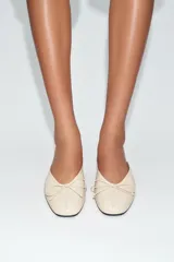 Zapatos de tacón tipo bailarina destalonada en piel color beige, con detalle de lazo en la parte delantera, tacón en bloque y punta redonda.