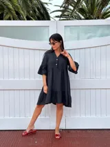 Vestido corto de lino color beige claro, con cuello mao, escote con botones de nácar, mangas tres cuartos con volados y ruedo con volado.