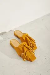 Zueco plano de cuero color dorado, con diseño de tiras anchas entrelazadas en el empeine y punta cuadrada.