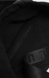 Tote bag negra de microfibra de alta densidad con diseño funcional. Presenta tiras de cinta de seguridad con logo grabado, sistema de elásticos laterales regulables para ajustar la silueta, bolsillo externo frontal con cierre y argolla metálica lateral.