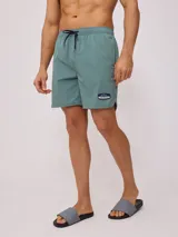 Short de baño tipo volley color verde azulado, con cintura elástica y cordón de ajuste en color azul marino. Presenta un parche con el logo de la marca en la pierna izquierda y aberturas laterales en el ruedo.