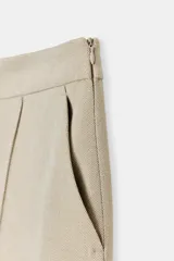Pantalón de vestir color beige claro, tiro alto, corte recto o ligeramente acampanado, con pinzas marcadas en el frente y bolsillos delanteros.