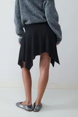 Minifalda negra de tiro medio con detalle de frunces en la cintura y bajo asimétrico con caída fluida.