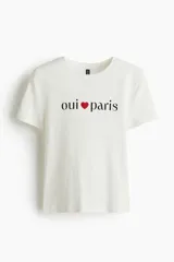 Remera de manga corta color blanco roto, con cuello redondo y estampado central con el texto "oui ❤ paris" en color negro y rojo.