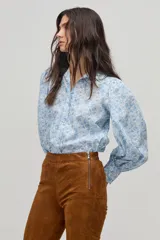 Camisa celeste con estampado floral en blanco, de corte clásico, cuello camisero y mangas largas abullonadas.