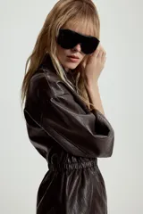 Chaqueta de efecto piel con cuello solapa, manga corta y cintura elástica. Presenta cierre frontal con cremallera y bolsillos decorativos en el frente.
