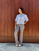 Camisa de corte recto y calce holgado, confeccionada en tela liviana color celeste con estampado de rayas verticales blancas con detalles de hojas. Presenta cuello en V, cierre frontal con botones de madera y mangas tres cuartos con terminación elástica.