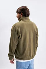 Buzo de polar verde militar con medio cierre frontal, cuello alto y bolsillo tipo canguro. Presenta un pequeño logo bordado en el pecho.