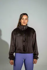 Buzo de plush color marrón, con cuello alto y cierre frontal parcial. Presenta un diseño holgado con puños elásticos y un pequeño bordado en el pecho.