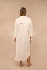 Vestido midi color crudo de estilo camisero, con cuello clásico, cierre frontal de botones, bolsillos laterales y mangas tres cuartos.