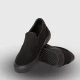 Zapatilla tipo slip-on de lona negra, con suela de goma vulcanizada al tono y detalle de relieve en el talón.