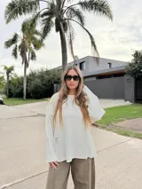 Sweater de punto con diseño bicolor y texturas combinadas, presenta un lado de tejido liso y otro con trenzado vertical. Posee cuello redondo, corte holgado y una etiqueta decorativa en el frente.