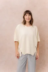 Buzo oversize color beige, con escote redondo, mangas cortas amplias de corte raglán y terminación frontal asimétrica en punta con aberturas laterales.