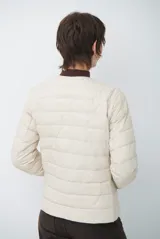 Campera acolchada tipo puffer en color beige, con diseño sin cuello y cierre frontal con botones a presión.