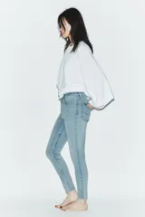 Jeans de tiro alto con corte skinny y largo tobillero. Presenta diseño clásico de cinco bolsillos, cierre frontal con cremallera y botón, con un acabado de lavado azul medio.