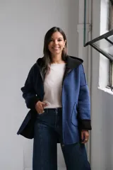Tapado de paño azul con capucha, diseño de corte holgado y largo a la cadera. Presenta detalles en color negro en el interior, bordes y puños, con bolsillos frontales amplios y cierre frontal.