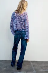 Top de punto fino color lila con estampado de flores abstractas en tonos azules y rojos, con cuello redondo y mangas largas acampanadas.