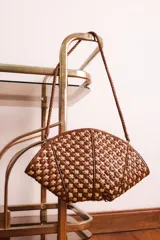 Cartera de mano con forma de hoja, confeccionada en cuero trenzado color naranja y negro. Asa corta trenzada de cuero negro.