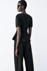 Top peplum confeccionado en hilatura de algodón de color bordó, con escote en V pronunciado, mangas cortas abullonadas y bajo con vuelo.
