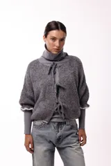Saco de punto gris con frente abierto, cierre mediante lazos frontales y mangas con puños elásticos. Presenta una textura suave y un diseño de volumen holgado.