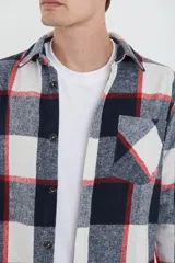 Sobrecamisa de tejido suave con diseño de cuadros en tonos azul marino, blanco y líneas rojas. Presenta cuello clásico, cierre frontal con botones, un bolsillo superior en el pecho y mangas largas con puños abotonados.