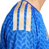Camiseta de fútbol Adidas de la selección italiana, modelo Local 26, color azul con patrón de hojas repetidas en tono más oscuro. Presenta cuello en V con ribete dorado y detalles dorados en los hombros y puños. Escudo de la FIGC y logo de Adidas en dorado en el pecho.