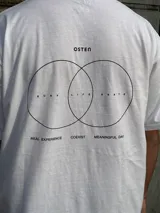 Remera blanca de corte oversize con estampado en la espalda que incluye dos círculos intersecados con las palabras 'Surf', 'Life' y 'Skate', y las frases 'Real Experience', 'Coexist' y 'Meaningful Day'.