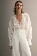 Jean de denim de algodón blanco con leve elasticidad, tiro alto y diseño de pierna ancha (wide leg). Cuenta con bolsillos de parche delanteros, botón metálico con diseño y pliegues marcados al frente y en la espalda.
