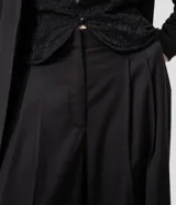 Pantalón de sastrería negro de modelado amplio, con pinzas frontales y cintura con pasadores.