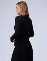 Vestido midi negro de tejido de punto, con escote en V cruzado, mangas largas, lazo en la cintura y apliques de perlas en el escote y la cintura.