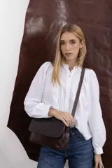 Cartera bandolera de cuero vacuno color marrón oscuro, con solapa frontal con textura efecto cocodrilo, costuras pespuntadas visibles y correa larga ajustable.