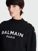 Sweatshirt negro Balmain Paris de corte cropped, con cuello alto y logo estampado en blanco. Presenta botones dorados en el hombro.