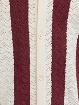 Polo de tejido estructurado con diseño de rayas verticales en colores bordó y blanco, cuello polo, mangas cortas y cierre frontal de botones.