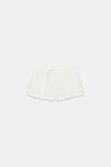 Short de tiro medio color blanco, confeccionado en mezcla de algodón y poliamida. Cuenta con cintura elástica con cordón de ajuste, bolsillos laterales y detalle de vuelta en el dobladillo.