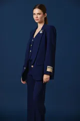 Saco de corte sastre en color azul marino, con solapas clásicas, cierre frontal de botones dorados y detalle de parche rectangular con inscripción en la manga izquierda.