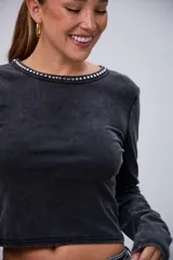 Remera negra de manga larga con efecto acid wash y cuello redondo decorado con tachas plateadas.