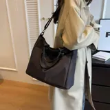 Bolso tipo tote y shopper de color negro, confeccionado en poliéster con amplio espacio interior, doble asa de mano y correa larga ajustable para llevar al hombro o cruzado.