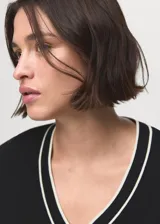 Jersey de punto fino de manga larga en color negro, con cuello en V y detalles de líneas blancas en contraste en el cuello y los puños.