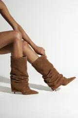 Bota de caña media confeccionada en gamuza color camel, con diseño fruncido, punta fina y taco aguja pequeño.
