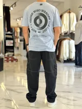 Remera oversize de color celeste con efecto gastado acid wash, mangas cortas y cuello redondo. Cuenta con un gran estampado circular en la espalda con la frase "Not all those who wander are lost" y texto adicional debajo.