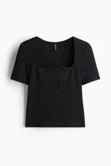Top negro de punto suave con escote cuadrado y mangas cortas. Presenta un diseño entallado con un detalle decorativo en forma de V realizado en broderie en el centro del busto.