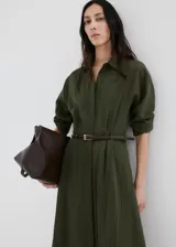 Vestido largo verde militar, con cuello camisero, cierre frontal con botones, mangas tres cuartos y diseño evasé. Incluye un cinturón fino de poliuretano con hebilla metálica.