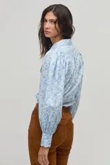 Camisa celeste con estampado floral en blanco, de corte clásico, cuello camisero y mangas largas abullonadas.