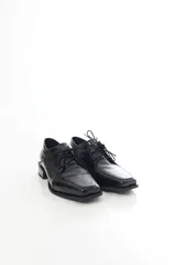 Zapato de charol negro de cuero vacuno con textura grabada tipo reptil, punta cuadrada y cordones al tono.