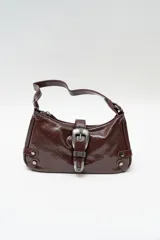 Bolso de hombro tipo baguette en color negro con acabado brillante. Presenta un diseño estructurado con una hebilla decorativa metálica en el frente y detalles de tachas plateadas en los laterales.