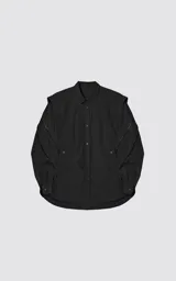 Chaqueta tipo overshirt de microfibra, color negro, con calce oversize y ruedo curvo. Presenta cierre frontal con broches a presión, bolsillos frontales de gran tamaño y cierres laterales a lo largo de las mangas para ajustar su amplitud.