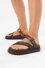 Sandalias de cuero color chocolate con acabado metalizado, diseño de tiras cruzadas, agarre en el dedo y hebilla metálica. Cuentan con base acolchonada y plataforma.