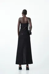 Vestido largo negro strapless con acabado brillante, corte ajustado en el torso y falda que cae recta con tajo frontal.